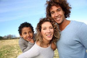 A family of three stand smiling in a field. They are feeling happier after beginning christian family therapy in Atlanta, GA with Faith and Family Empowerment.