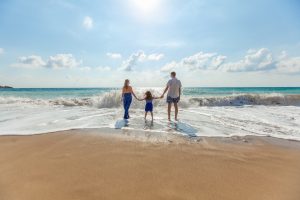 A family of three walks on the beach holding hands. They are feeling much happier after beginning christian family therapy in Atlanta, GA with Faith and Family Empowerment.