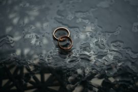 Two wedding bands sit on top of each other on the ground in the rain. The couple the rings belong to regret not starting marriage counseling in Atlanta, GA with Faith and Family Empowerment.
