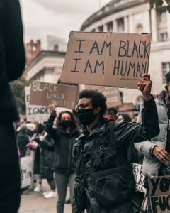 A group of people are participating in a Black Lives Matter protest. The photo zooms in one man, wearing a mask and holding a sign. He has gained the confidence to stand up for what he believes in after starting black men therapy in Atlanta, GA with Faith and Family Empowerment.