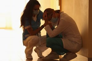 A nurse offers support to a doctor sitting against a wall with a mask on. Depression counseling in Atlanta, GA can offer support with pandemic related anxiety. Learn more about anxiety treatment in Decatur, GA or depression treatment in Norcross, GA.