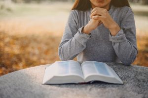 Shows a woman reading the Bible and praying. Represents how working with a christian counselor in atlanta, ga will support you with managing your anxiety and implement your religion while doing it.