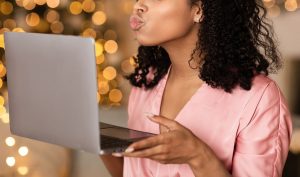 Shows a woman blowing a kiss to her laptop camera. Represents how a marriage counselor in atlanta, ga can support your relationship through online therapy in georgia.