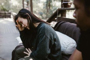 A distressed woman sits with her hand on her forehead while talking to someone, representing the emotional challenges addressed through EMDR therapy in Atlanta and the supportive process of premarital counseling in Atlanta, GA.