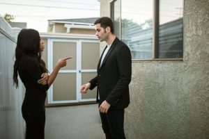 A couple stands outside in tense conversation; the woman points her finger while the man looks down, highlighting the emotional disconnection that can stem from imposter syndrome in relationships in Atlanta, GA.
