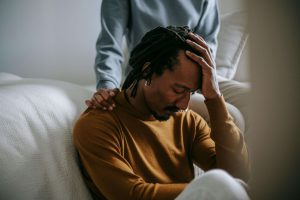 A distressed man sits with his head in his hand while his partner offers comfort—a moment reflecting the emotional toll before seeking marriage counseling or divorce in Atlanta and support from a premarital counselor in Atlanta, GA.