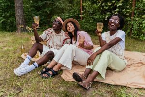 Three friends enjoying a joyful picnic outdoors, holding amber glasses and laughing together. Perfect for a blog on finding an EMDR therapist in Atlanta and a marriage counselor in Atlanta, GA, to rebuild trust and connection after betrayal.