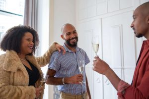 Three people share a joyful moment indoors, holding champagne flutes and smiling warmly. A Black therapist in Decatur, GA, and online Christian counseling in Atlanta, GA, can help foster confidence and healthy boundaries in relationships.