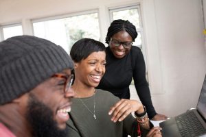 Three individuals laughing together while looking at a laptop, symbolizing the supportive guidance of a Black therapist in Decatur, GA, and the healing power of EMDR therapy in Atlanta to overcome inner critic patterns.