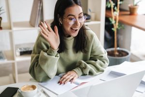 A college student smiles and waves during a video call with an emdr therapist in atlanta, meeting with an online therapist in decatur, ga and staying connected through online therapy atlanta while home on break.