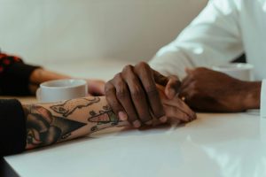Couple holding hands across a table with coffee cups, representing connection and healing through black marriage counseling in decatur, ga and online marriage counseling in atlanta, ga for those recovering from church hurt.