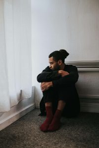 Man sitting alone on bedroom floor looking distressed, representing the pain of church hurt and spiritual trauma that a black christian therapist atlanta can address through marriage counseling or divorce in atlanta support services.