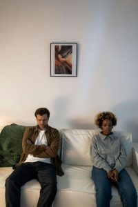 An interracial couple sitting apart on a white couch with closed-off body language and visible tension, illustrating the emotional distance that can be addressed through Decatur marriage counseling with a Christian therapist in Decatur, GA