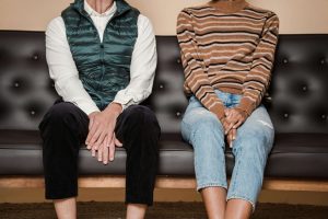 A couple sitting apart on a couch with visible tension and distance between them, representing the emotional disconnect that can be healed through affair recovery in Decatur, GA with a Black Christian therapist Atlanta