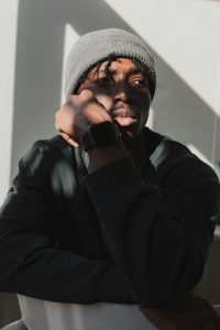 A young Black man in a gray beanie looking upward with hand near face in contemplative pose, representing the mental health struggles college students face that can be addressed through anxiety treatment Decatur with a therapist for Black men Decatur