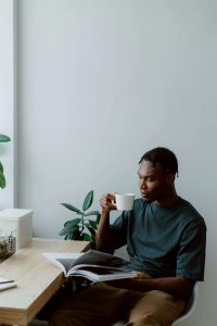 A young Black man in a teal shirt sits quietly in a chair reading a magazine and holding a cup, representing the peace and clarity that becomes possible through working with a therapist for black men decatur and therapy for black men decatur, ga