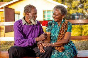 An older Black woman and a young Black man lean together against a red wall smiling while looking at a phone, representing the family connection and generational bonds that christian counseling in decatur, ga and anxiety treatment decatur at Faith and Family Empowerment can help families protect and strengthen.