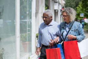 An older interracial couple walks together along a sunny street carrying colorful shopping bags and sharing a quiet moment of connection, representing the everyday intentionality that christian counseling in decatur, ga and marriage counseling in decatur, ga at Faith and Family Empowerment can help couples rediscover.