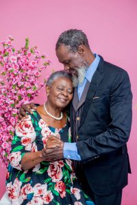 An older Black couple embraces warmly against a pink floral backdrop, representing the deep intimacy and lasting connection that marriage counseling in decatur, ga and a marriage counselor decatur ga can help couples rebuild.