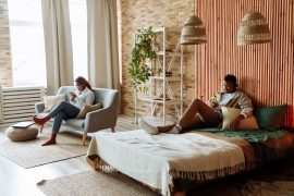 A Black couple sits on opposite sides of a room scrolling their phones separately, representing the parallel living and sexual drift that marriage counseling in decatur, ga and a marriage counselor decatur ga can help couples address.