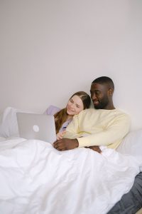 A Black couple sits together at a table with a laptop nearby as the woman rests her head on her partner's shoulder in a quiet moment of connection, representing the everyday intimacy that christian marriage counseling in norcross, ga and online therapy in georgia at Faith and Family Empowerment can help couples nurture.