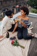 An interracial couple toasts wine glasses during a rooftop picnic with roses and grapes, representing the intentional connection that a marriage counselor decatur ga and marriage intensive decatur at Faith and Family Empowerment can help couples rediscover.