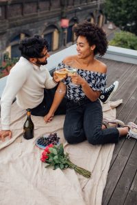 An interracial couple toasts wine glasses during a rooftop picnic with roses and grapes, representing the intentional connection that a marriage counselor decatur ga and marriage intensive decatur at Faith and Family Empowerment can help couples rediscover.